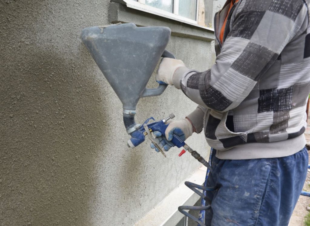 Man Spaying stucco texture on exterior of house