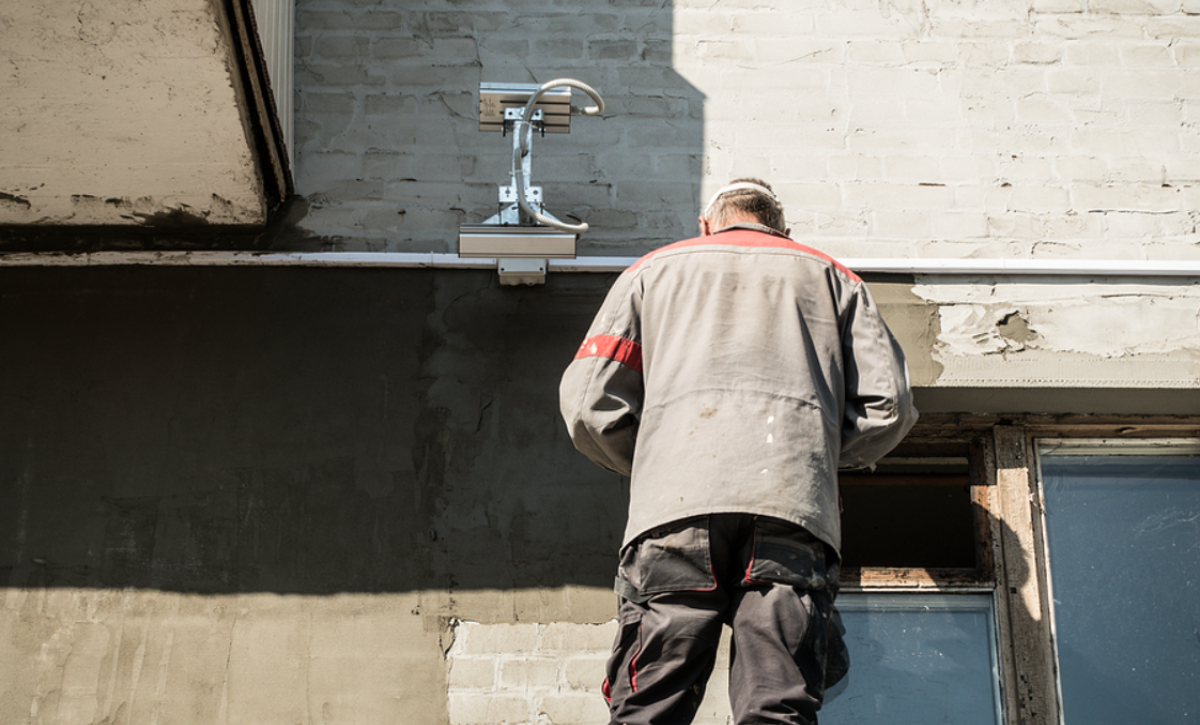worker is repairing the building from the outside. man fixing the wiring and plastering the walls, Exterior Stucco Repair